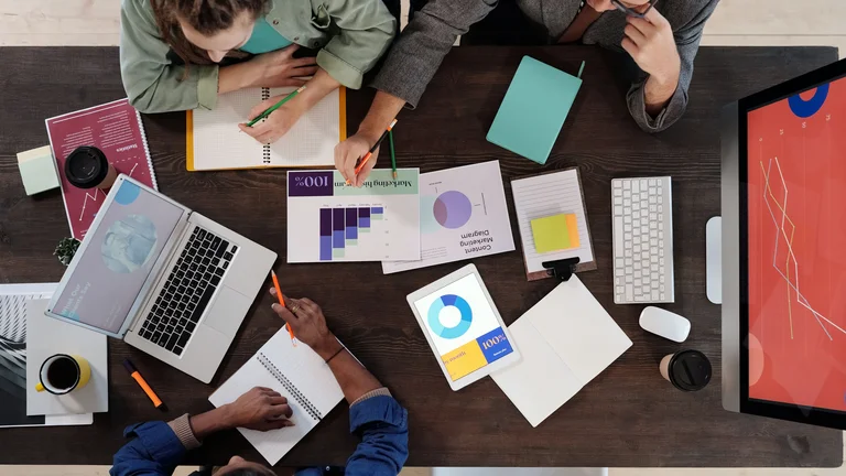 birds-eye view of people working at a desk with laptop and notepads