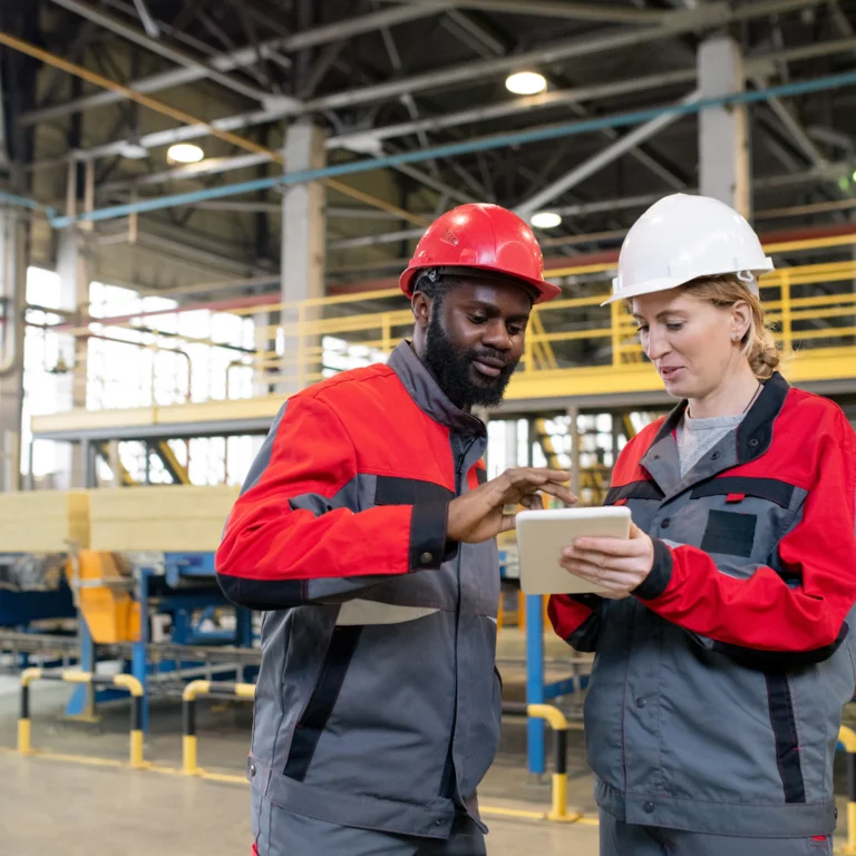 Diverse team of construction professionals with tablet in factory setting, engaging in CDM-focused planning and risk assessment discussion